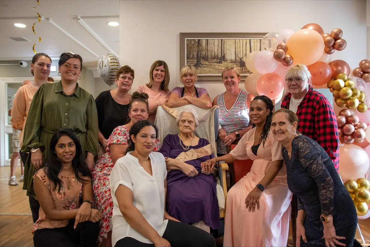 A resident with the care team among pink and gold balloons at a birthday celebration.