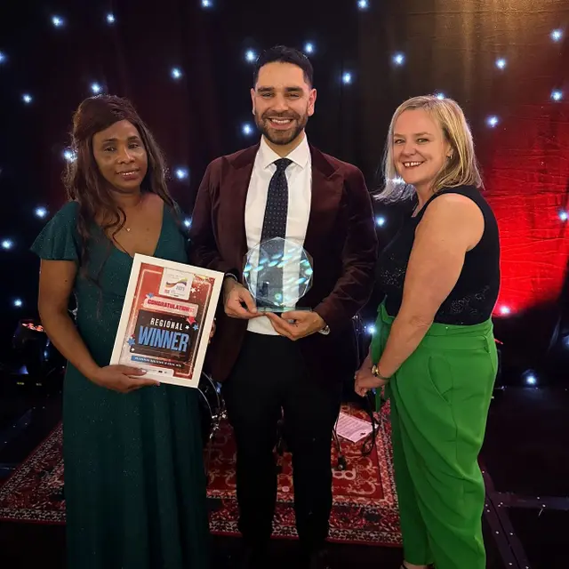Three people from Aria on stage with the trophy and the winner's certificate.