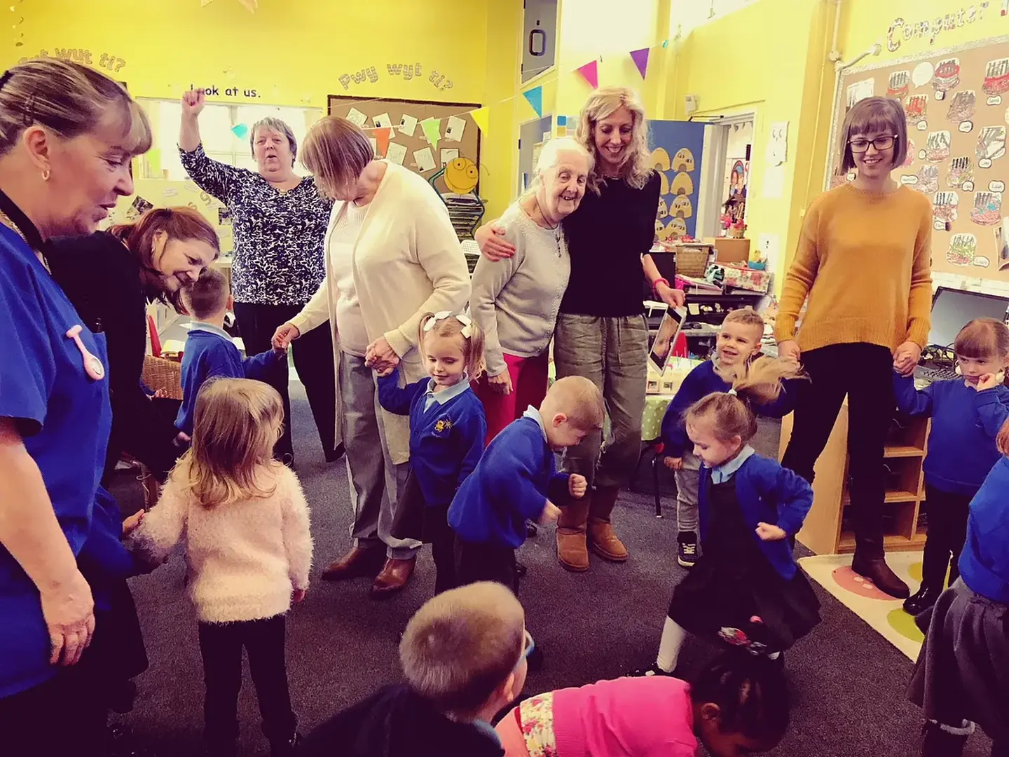 Residents and pupils dancing together in a classroom at Malpas Court Primary School.