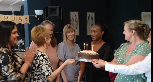 Team members carrying a lit birthday cake into the lounge.
